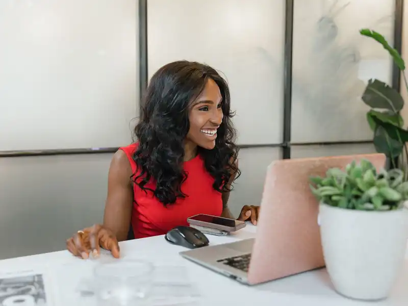 A smiling business owner at her laptop with her phone
