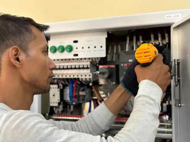 An electrician working on a breaker panel with a drill
