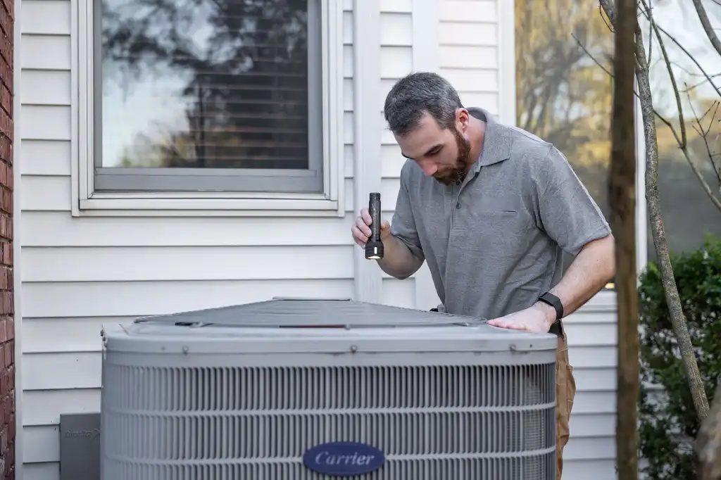 A technician inspecting an outdoor air conditioning unit beside a house