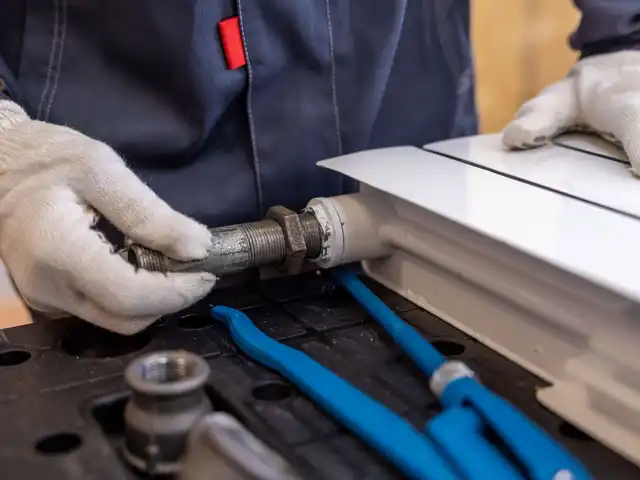 A plumber in gloves fitting a radiator pipe
