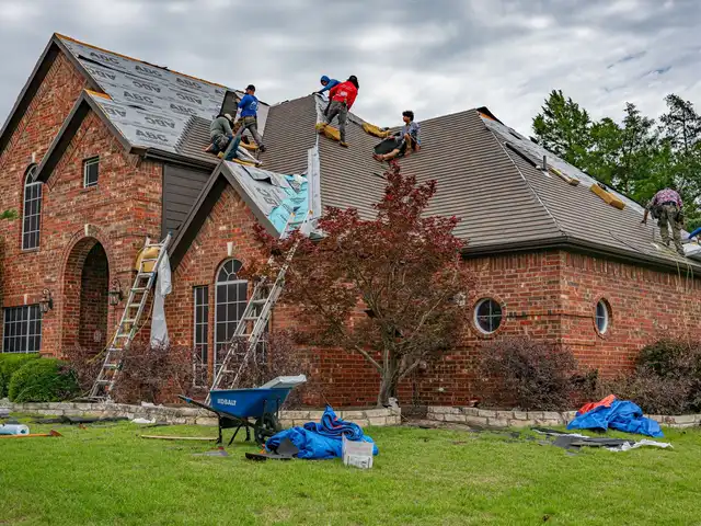 Roofers replacing shingles on a brick house