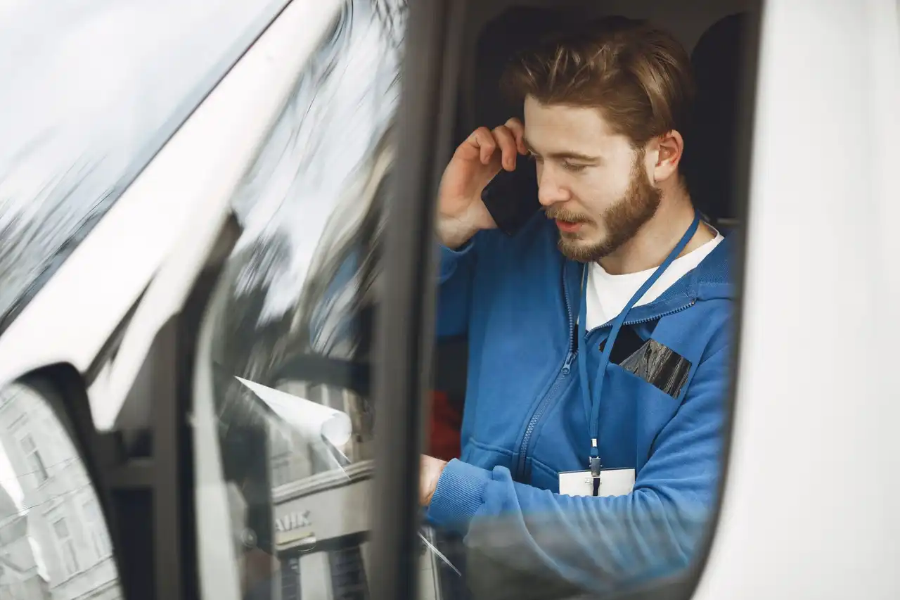 A tradesman in a blue work jacket taking a call in his van