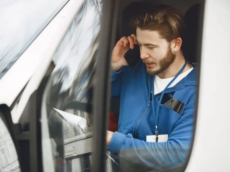 A tradesman in a blue work jacket taking a call in his van